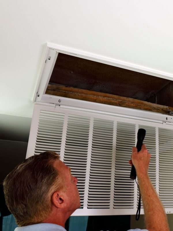 An HVAC technician is looking into an air vent. 