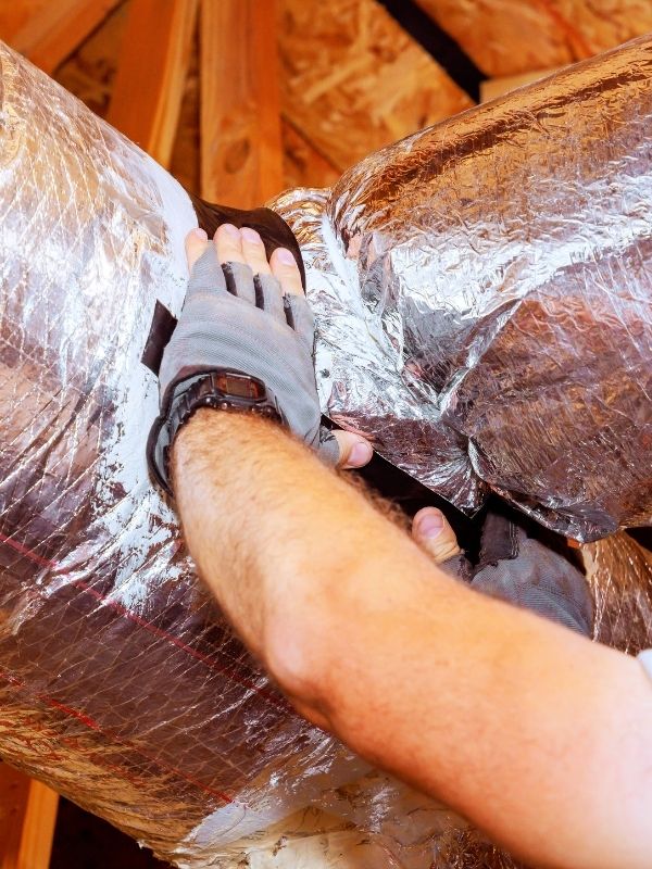 An HVAC technician is working on an air duct. 