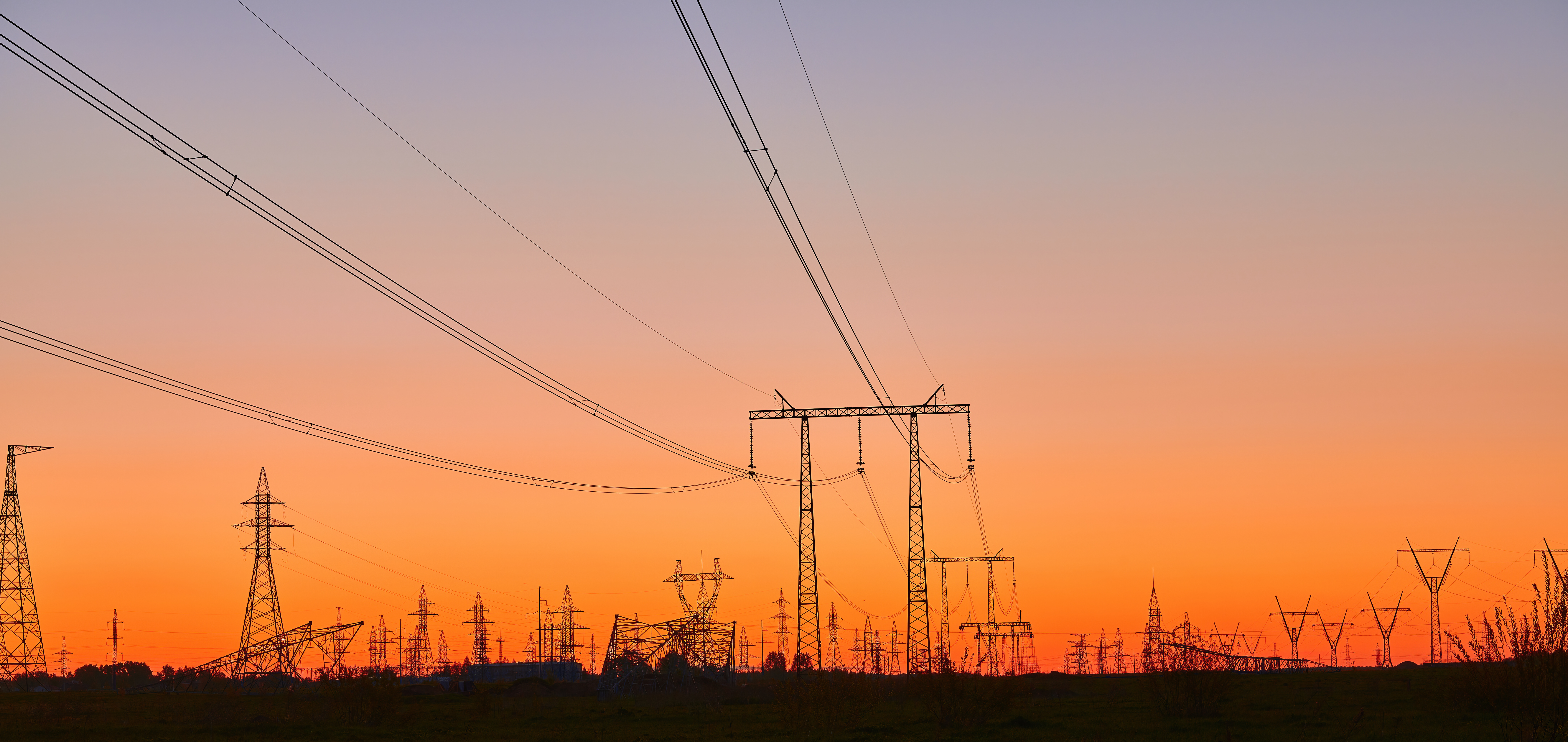 High voltage electricity towers on field at sunset.